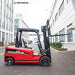 Full left side profile of a 6,500 lb 60V battery electric forklift with three-stage mast, extended 48-inch pallet forks, and deep-tread rubber tires, parked on concrete outside a modern distribution center.