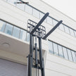 Close-up low-angle shot of 48-inch steel pallet forks on the carriage of a 6,500 lb electric forklift, showing lift chains, hydraulic cylinder, and welded mast rails for heavy warehouse load handling.