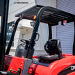Operator compartment of a 7700 lb electric forklift showing overhead guard, adjustable seat, steering wheel, and hydraulic control levers