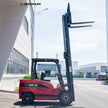 Right side profile of a 7700 lb electric forklift with elevated mast and horizontal forks in an industrial yard