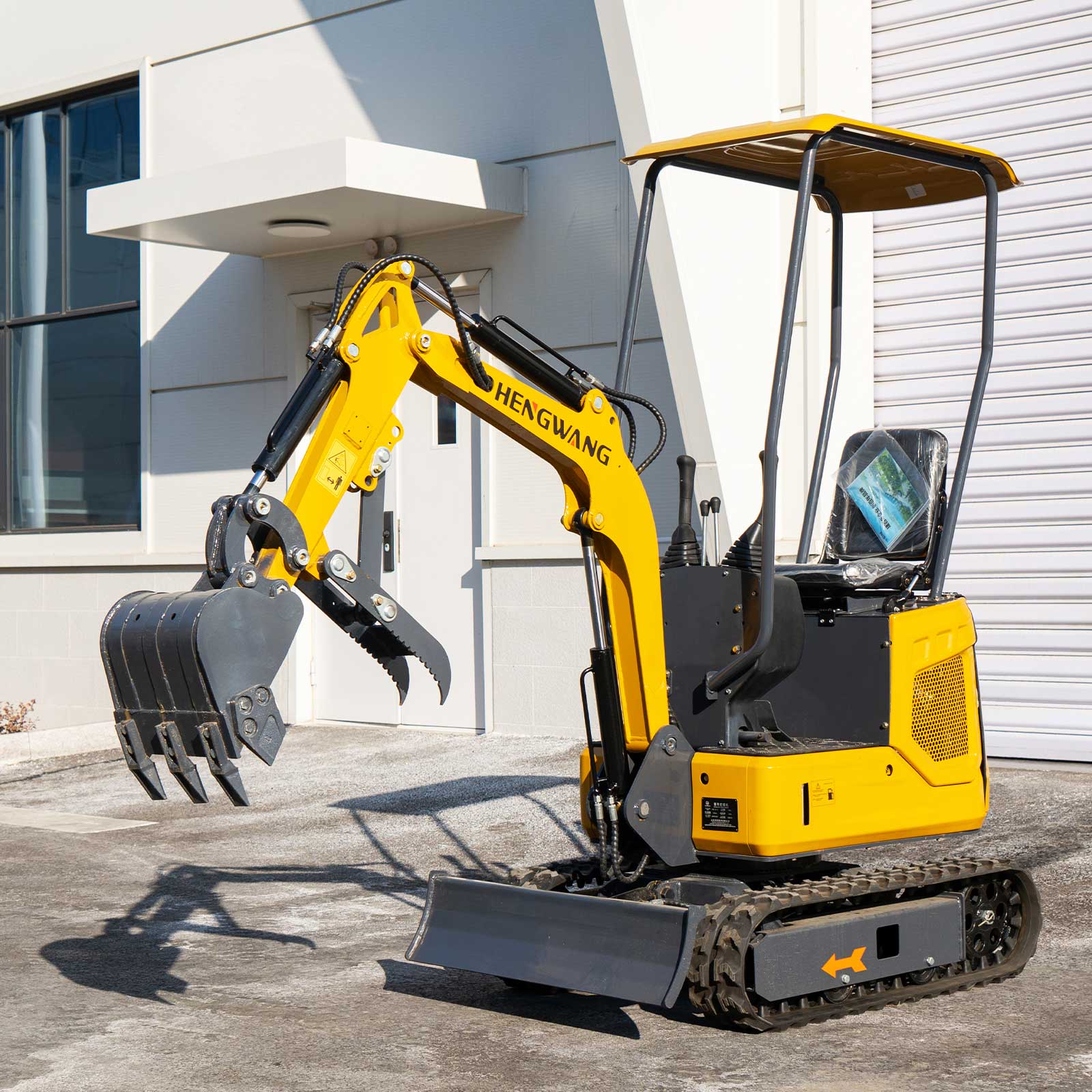 Yellow HENGWANG mini crawler excavator with standard digging bucket and ripper claw, compact small digger with rubber tracks and sun canopy, outdoor factory front shot