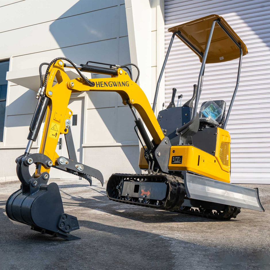 Side view of HENGWANG yellow mini crawler excavator with digging bucket and ripper attachment, rubber tracks and sun roof canopy, compact small digger parked outside factory building